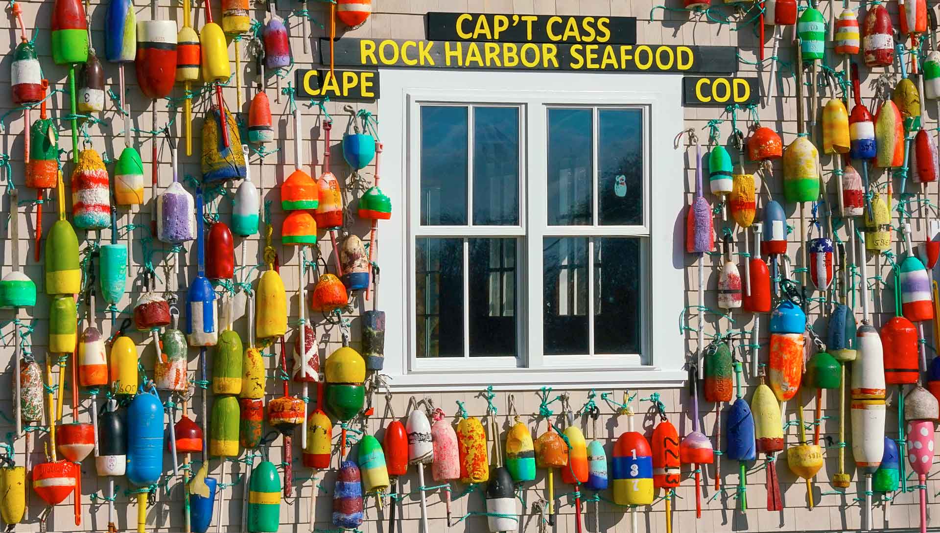 The west side of Cap't Cass Restaurant showing colorful lobster buoys hung in front of the shingles        